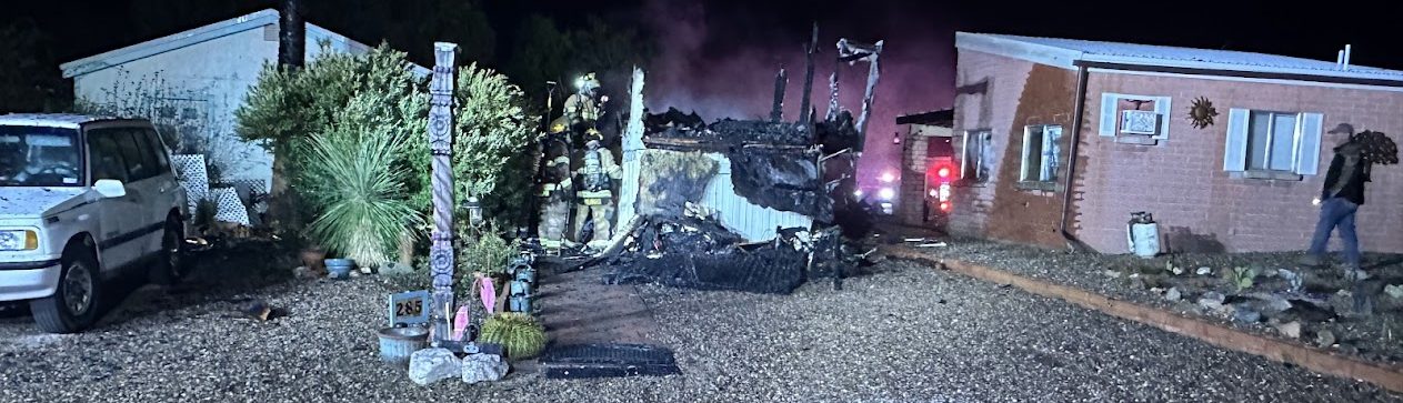 Fire apparatus and responders at a nighttime emergency scene, with hose lines across the foreground.